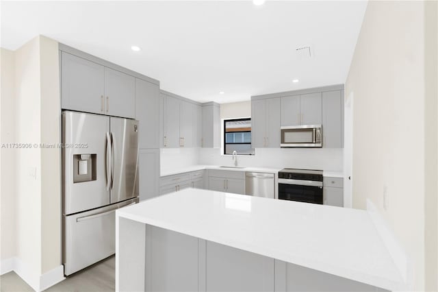 kitchen with appliances with stainless steel finishes, gray cabinets, sink, and kitchen peninsula