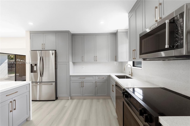 kitchen with gray cabinets, appliances with stainless steel finishes, sink, and light hardwood / wood-style flooring