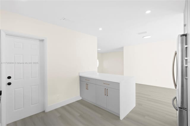 kitchen featuring light hardwood / wood-style floors, gray cabinetry, stainless steel refrigerator, and kitchen peninsula