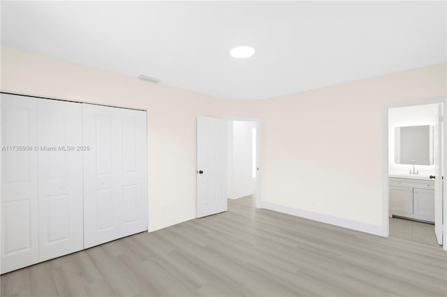 unfurnished bedroom with ensuite bathroom, light wood-type flooring, and a closet