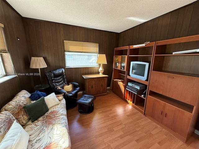 living room featuring a textured ceiling, light hardwood / wood-style floors, and wood walls