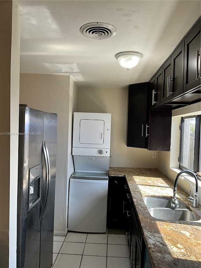 kitchen with sink, stacked washing maching and dryer, stainless steel fridge with ice dispenser, and light tile patterned floors