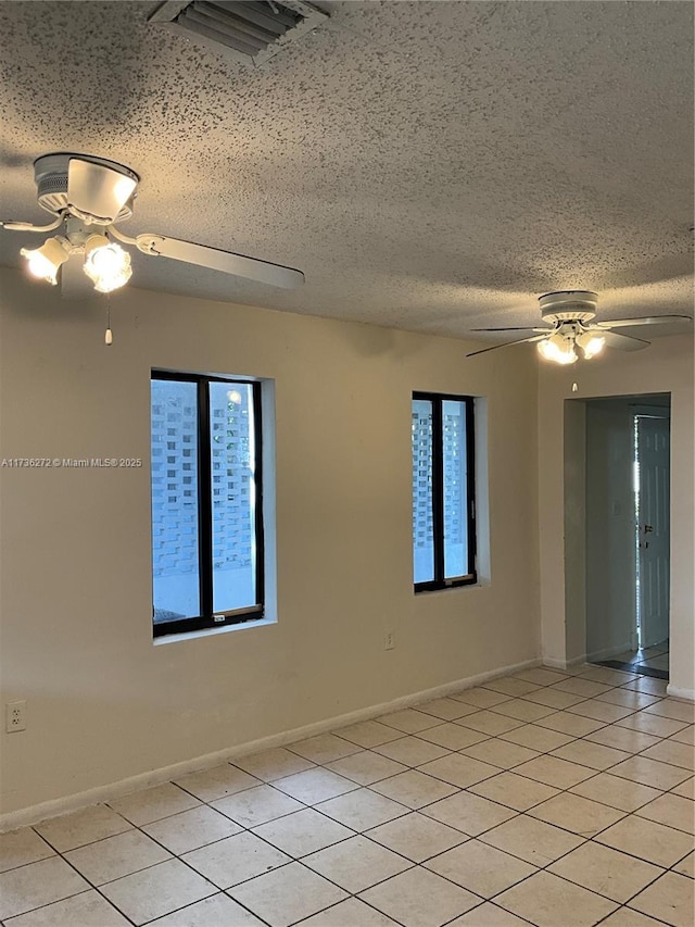 tiled spare room featuring ceiling fan, a wealth of natural light, and a textured ceiling