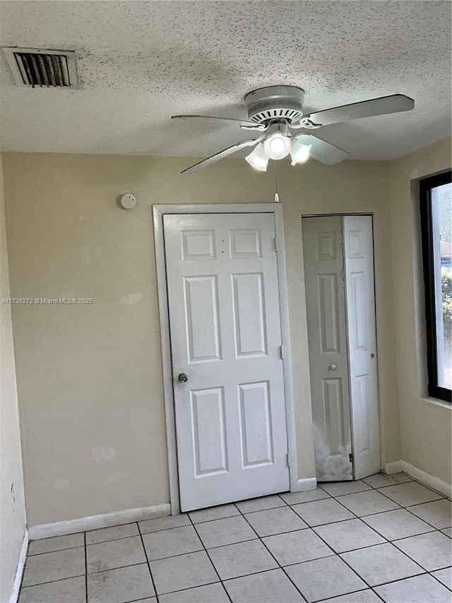 unfurnished bedroom with ceiling fan, a textured ceiling, a closet, and light tile patterned floors