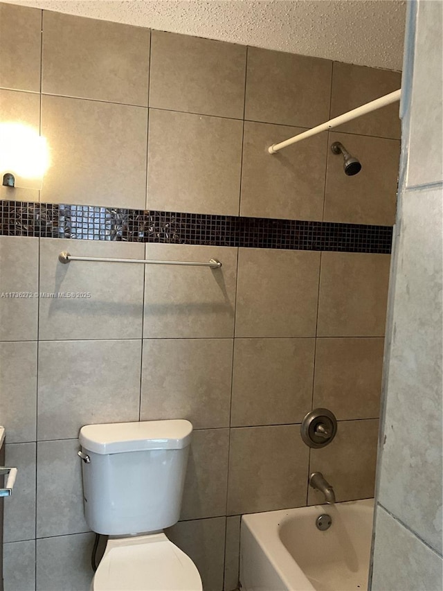 bathroom featuring tiled shower / bath, toilet, and tile walls