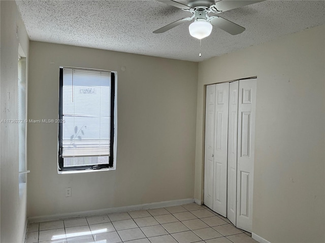 unfurnished bedroom with light tile patterned floors, a closet, a textured ceiling, and ceiling fan