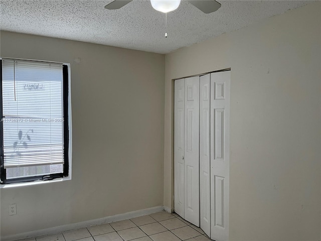 unfurnished bedroom with light tile patterned flooring, ceiling fan, a textured ceiling, and a closet