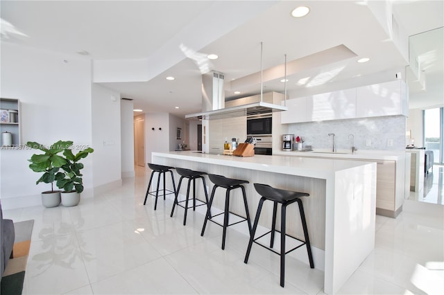 kitchen with sink, a breakfast bar area, a spacious island, tasteful backsplash, and white cabinets