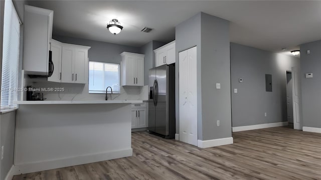 kitchen with stainless steel fridge, backsplash, light hardwood / wood-style floors, white cabinets, and kitchen peninsula