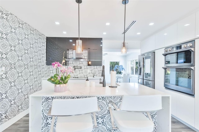 kitchen with decorative light fixtures, a kitchen breakfast bar, decorative backsplash, stainless steel appliances, and wall chimney range hood