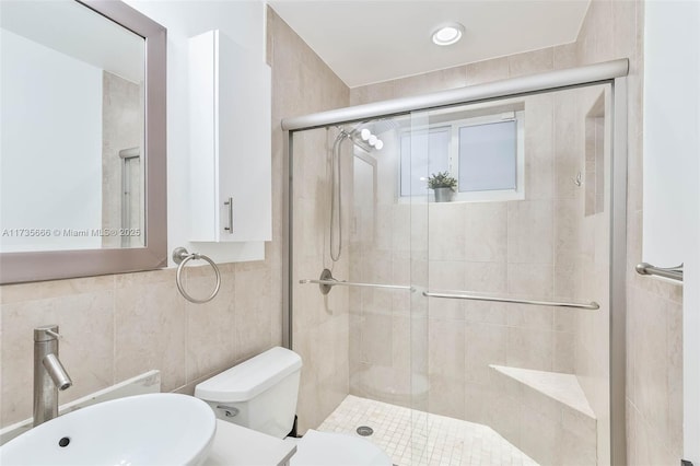 bathroom featuring walk in shower, toilet, sink, and tile walls