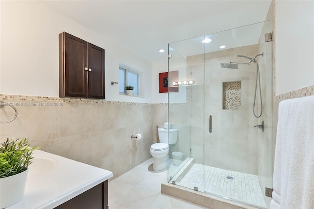 bathroom featuring vanity, toilet, a shower with door, and tile walls