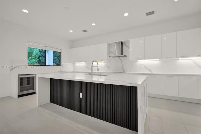 kitchen with wall chimney exhaust hood, sink, white cabinetry, a kitchen island, and beverage cooler