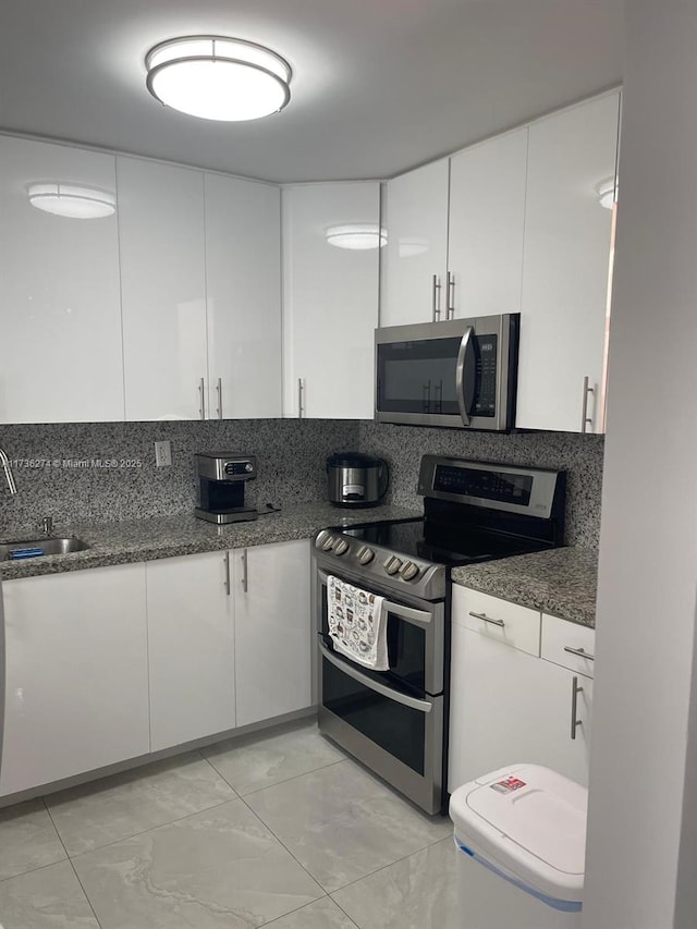 kitchen featuring appliances with stainless steel finishes, tasteful backsplash, white cabinetry, sink, and dark stone counters