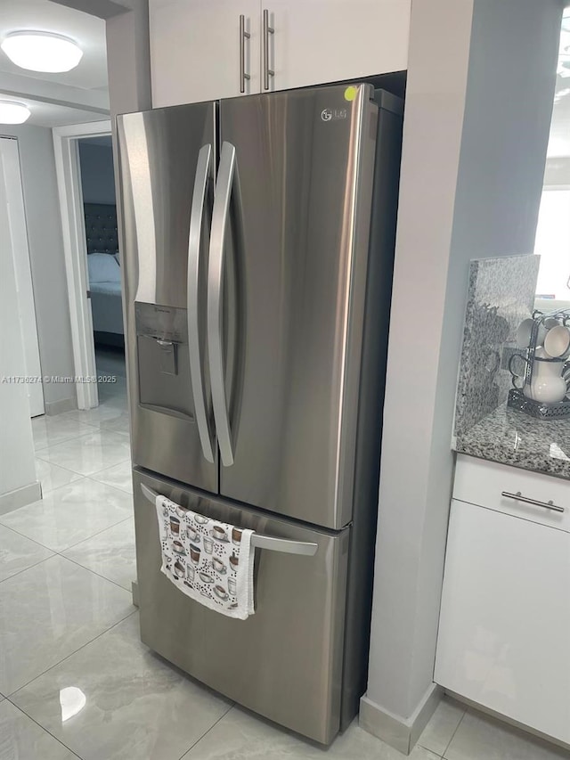 kitchen with stainless steel refrigerator with ice dispenser, white cabinetry, and light stone counters