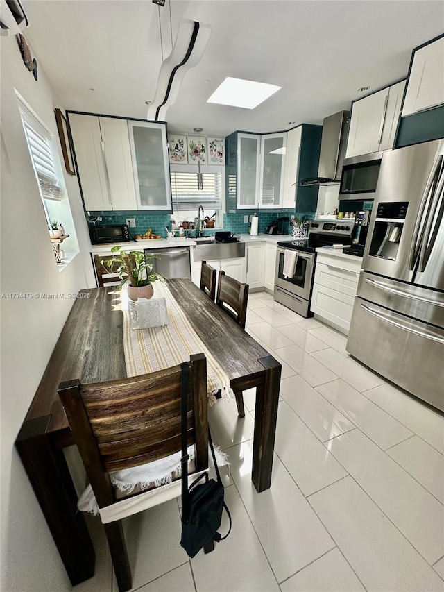 kitchen featuring stainless steel appliances, white cabinetry, tasteful backsplash, and wall chimney range hood