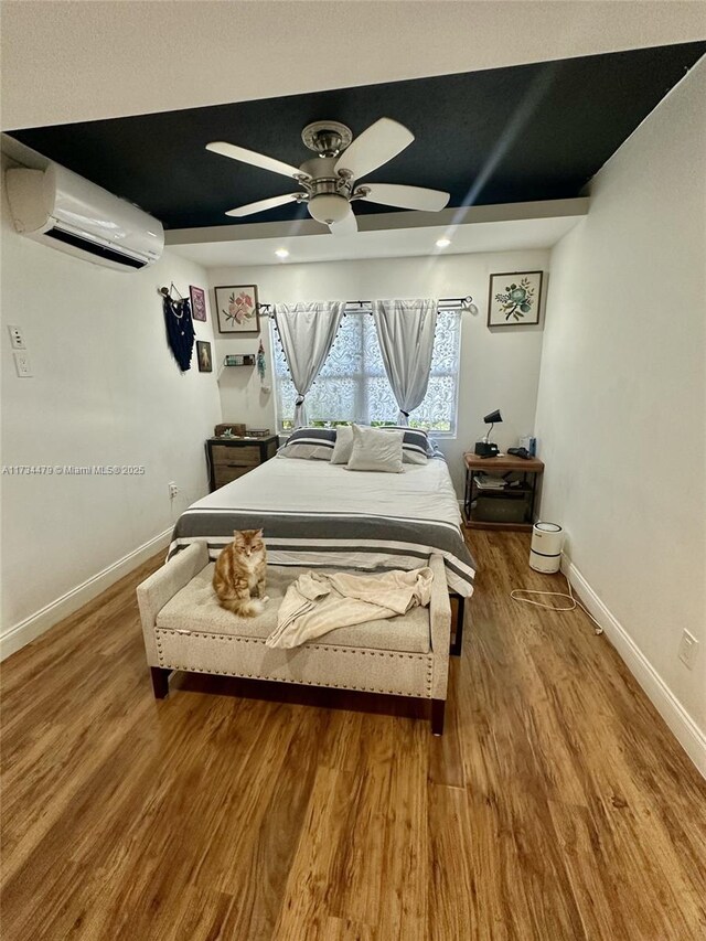 bedroom featuring hardwood / wood-style flooring, a wall unit AC, and ceiling fan