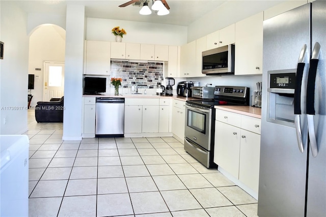 kitchen with light tile patterned floors, arched walkways, decorative backsplash, appliances with stainless steel finishes, and white cabinetry