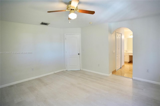 spare room featuring light wood-type flooring, baseboards, visible vents, and arched walkways