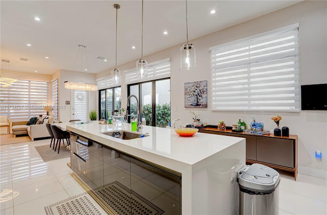 kitchen with light tile patterned flooring, decorative light fixtures, a sink, light countertops, and a center island with sink