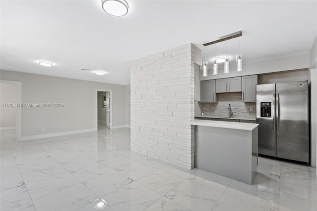 kitchen with gray cabinets, pendant lighting, sink, backsplash, and stainless steel fridge with ice dispenser