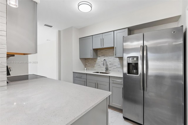 kitchen featuring sink, backsplash, gray cabinets, and stainless steel refrigerator with ice dispenser