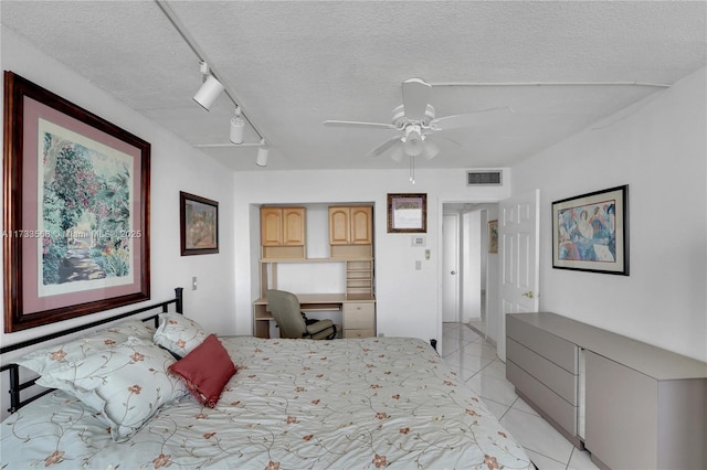 tiled bedroom with ceiling fan, built in desk, track lighting, and a textured ceiling