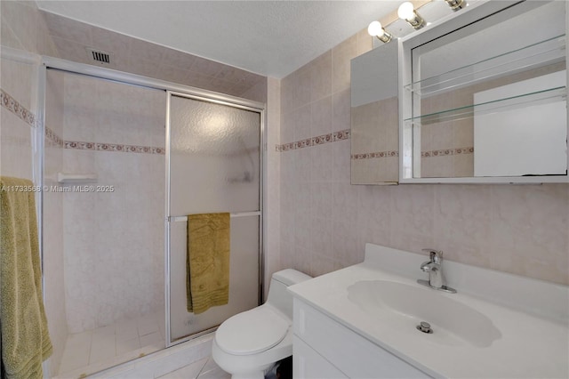 bathroom with toilet, a shower with shower door, tile walls, a textured ceiling, and vanity