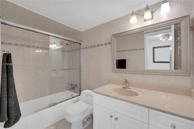 full bathroom with vanity, bath / shower combo with glass door, tile walls, and toilet