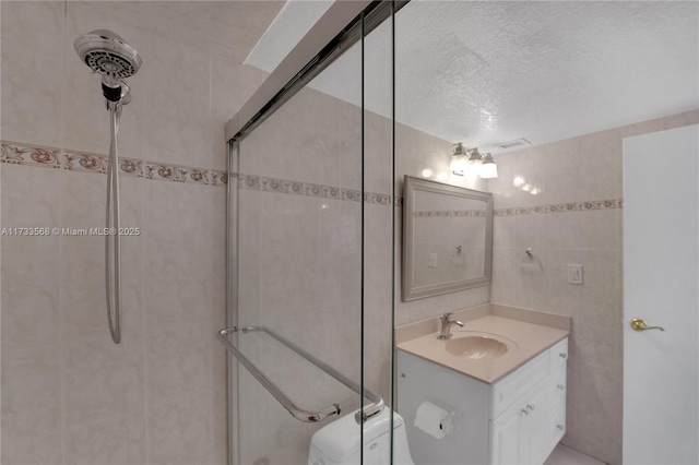 bathroom featuring tile walls, vanity, a tile shower, a textured ceiling, and toilet