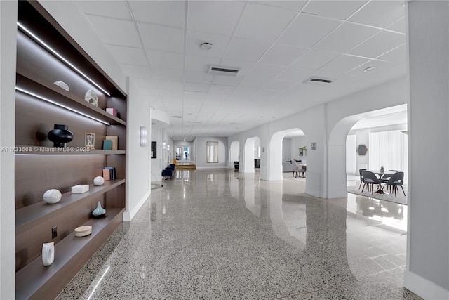 hallway with built in shelves and a paneled ceiling