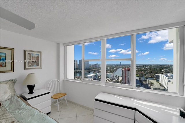 bedroom with multiple windows, light tile patterned floors, a textured ceiling, and a water view