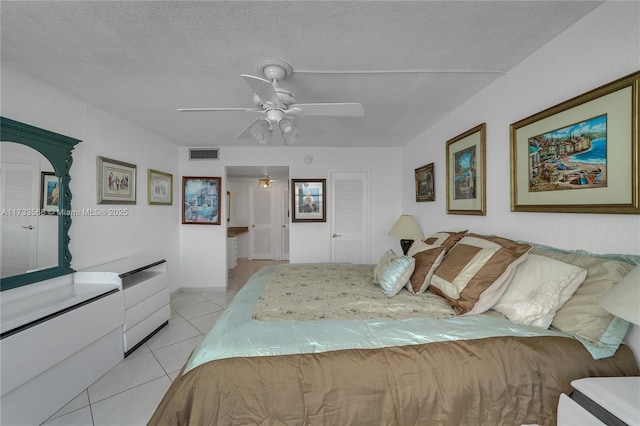 bedroom with light tile patterned flooring, ensuite bathroom, ceiling fan, and a textured ceiling