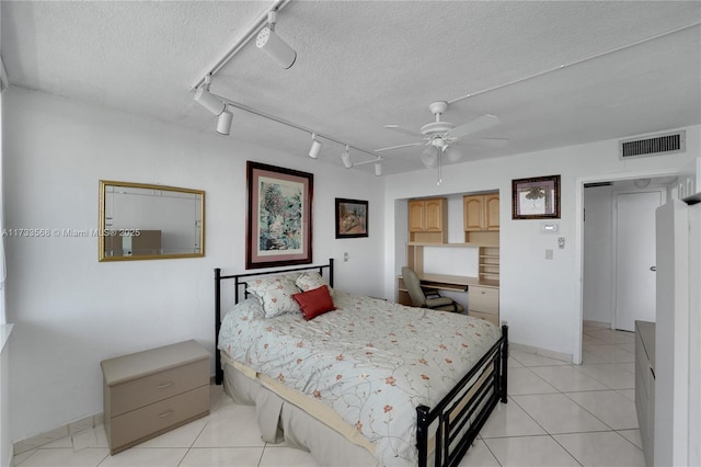 tiled bedroom with ceiling fan, built in desk, a textured ceiling, and track lighting