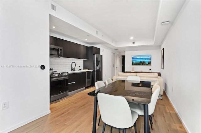 dining room with sink, a raised ceiling, and light wood-type flooring