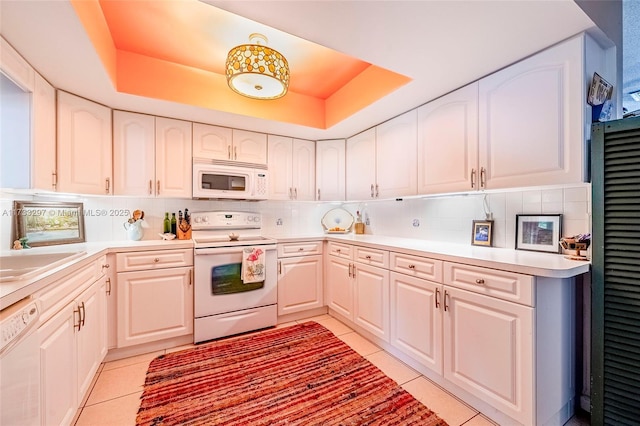 kitchen with light tile patterned flooring, white appliances, a raised ceiling, and backsplash