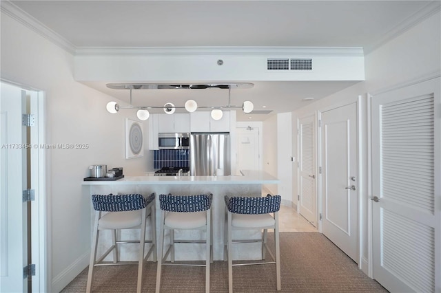 kitchen featuring a breakfast bar, ornamental molding, appliances with stainless steel finishes, kitchen peninsula, and white cabinets