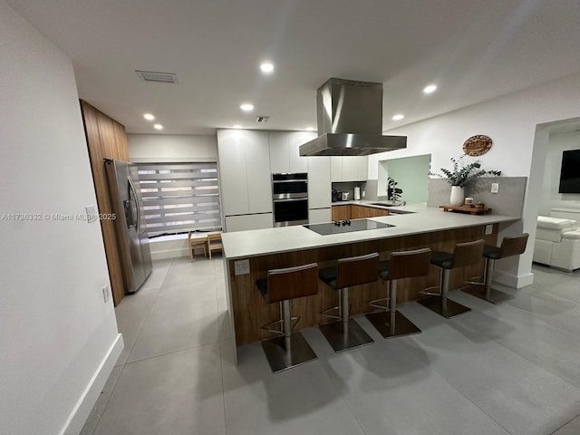 kitchen featuring a breakfast bar, white cabinetry, appliances with stainless steel finishes, kitchen peninsula, and island exhaust hood