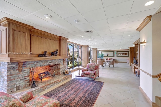 living room featuring a fireplace, a drop ceiling, and light tile patterned floors