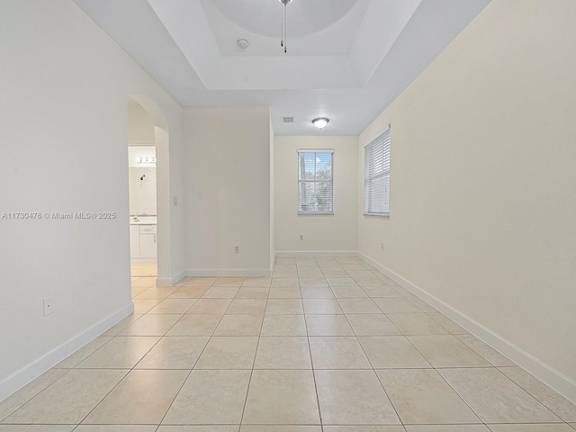 empty room with light tile patterned floors and a tray ceiling