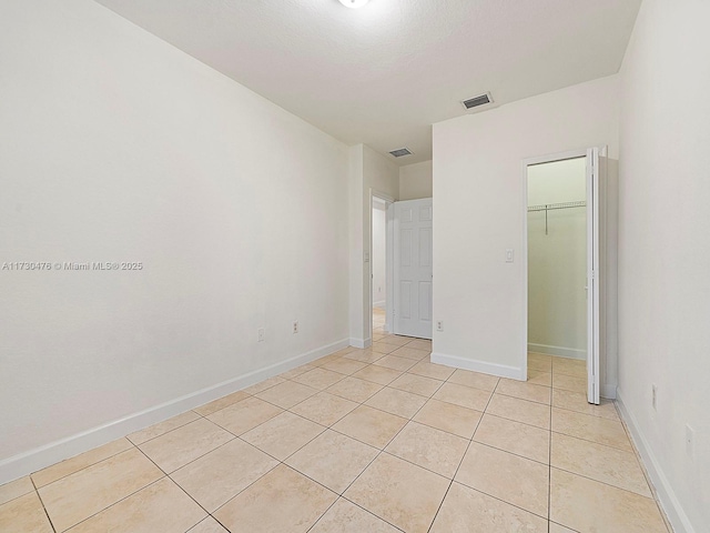 unfurnished bedroom featuring a spacious closet, light tile patterned floors, and a closet