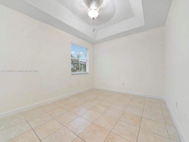 tiled empty room with ceiling fan and a tray ceiling