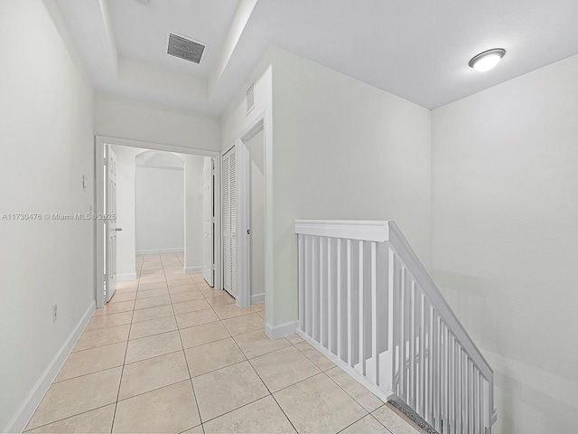 corridor featuring a raised ceiling and light tile patterned floors