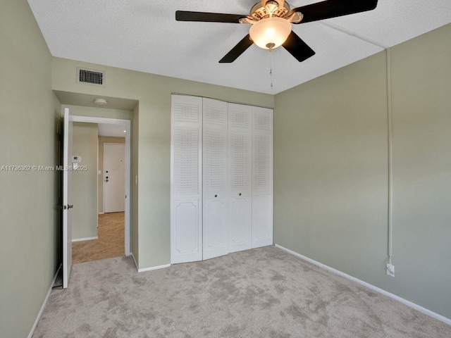 unfurnished bedroom with ceiling fan, light colored carpet, a closet, and a textured ceiling