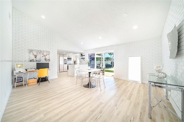 living room with lofted ceiling, brick wall, a textured ceiling, and light wood-type flooring