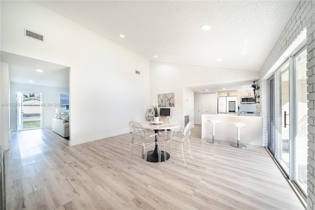 dining area with high vaulted ceiling, light hardwood / wood-style floors, a textured ceiling, and brick wall