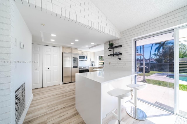 kitchen with lofted ceiling, a kitchen breakfast bar, kitchen peninsula, stainless steel appliances, and light wood-type flooring