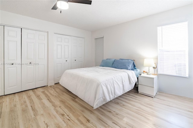 bedroom with ceiling fan, two closets, light hardwood / wood-style flooring, and a textured ceiling