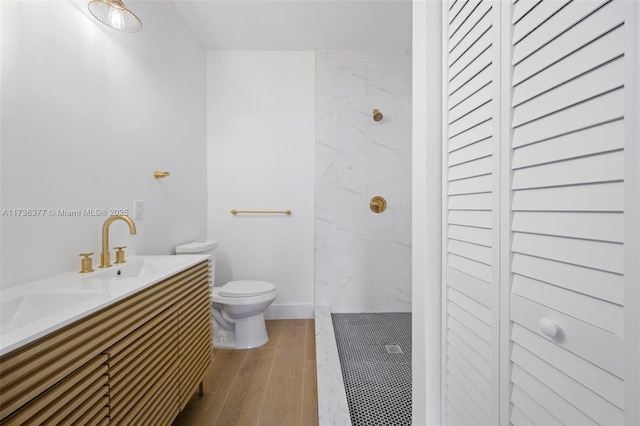 bathroom featuring wood-type flooring, a tile shower, vanity, and toilet