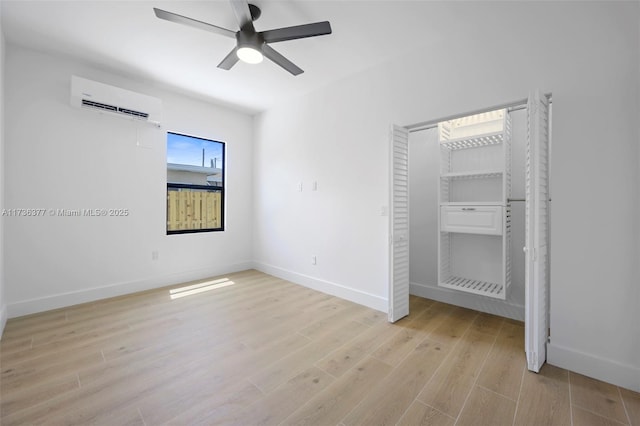 unfurnished bedroom with ceiling fan, a wall mounted AC, and light wood-type flooring